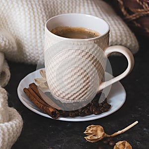 A cup of coffee is the key to a good mood. On a black, dark textural background, a composition of white, cream scarf and a white