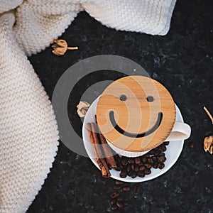 A cup of coffee is the key to a good mood. Wooden smiley on a dark, black, textural background. On the table there is a white,