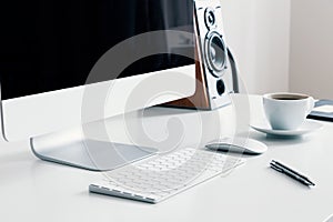 Cup of coffee, keyboard and desktop computer on desk in white home office interior. Real photo photo