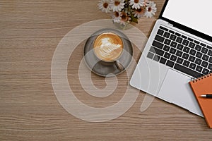 Cup of coffee, laptop computer, notebook and flower pot on wooden table.