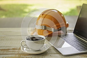 Cup of coffee,  ,laptop computer and orange safety helmet  on wood table background in office workplace