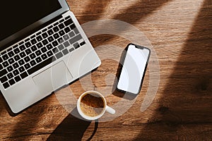 Cup of coffee, laptop computer and smartphone with blank white mockup screen on office work desk