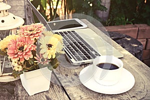 A cup of coffee and laptop on wood floor with flower
