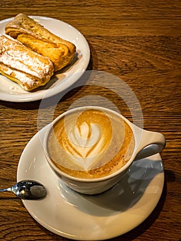 Cup of coffee latte with eclairs cakes on a wooden table. tasty breakfast