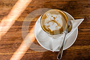 Cup of coffee latte with latte art of a bear holding a love heart, on the wooden table.