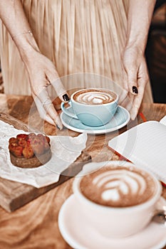 Cup of coffee latte and sweet pastry on wooden table in woman hands. Gentle romantic mood, girl wearing pink skirt