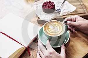 Cup of coffee latte on wooden table or background in woman hands from above. Having lunch in cafe.