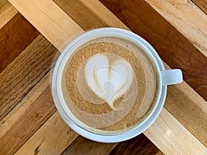 A cup of coffee latte on a wooden table. A mug of flat white coffee on a wooden background. Coffee art. Heart flower