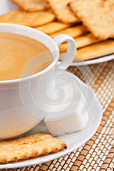 A cup of coffee with a lump sugar and crackers
