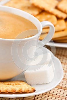 A cup of coffee with a lump sugar and crackers