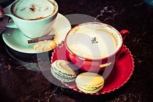 Cup of coffee with macaroon on table. Red cup of cappuccino and saucer with macaroon cookie on desk