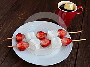 A cup of coffee and marshmallows with fresh strawberries on skewer