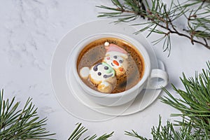 Cup of coffee with marshmallows. Marshmallow snowman in a Santa Claus hat. Winter drink in the snow. Christmas tree. Top