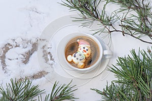 Cup of coffee with marshmallows. Marshmallow snowman in a Santa Claus hat. Winter drink in the snow. Christmas tree. Top