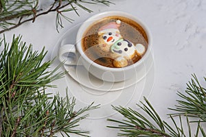 Cup of coffee with marshmallows. Marshmallow snowman in a Santa Claus hat. Winter drink in the snow. Christmas tree. Top