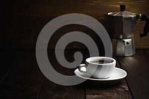 Cup of coffee with metal coffee percolator on dark wooden background