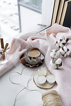 Cup of coffee with milk, candy, heart of rope, candles, cotton twig, knitted sweater, krini on the windowsill