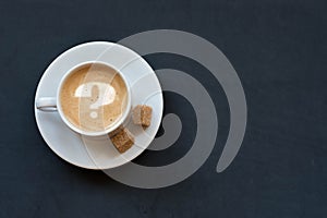 Cup of coffee with milk, cane sugar and question mark on dark background. Top view. Copy space