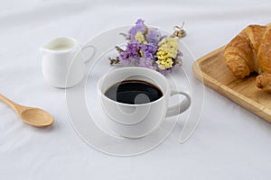 A cup of coffee, milk and croissant with statice flower