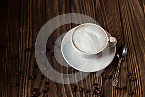 A Cup of coffee with milk and foam, coffee beans on a dark wooden background. selective focus