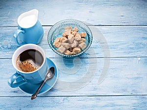 Cup of coffee, milk jug and cane sugar cubes.