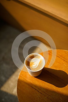 Cup of coffee with milk put on a chair in sunlight shade cafe with cozy room