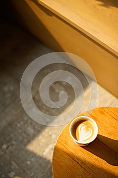 Cup of coffee with milk put on a chair in sunlight shade cafe with cozy room