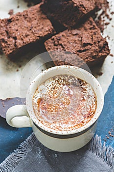 A cup of coffee with milk is sprinkled with cocoa powder and pieces of chocolate cake.