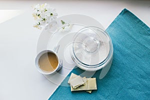 Cup of coffee with milk, sugar, white chocolate, flowers and a blue napkin
