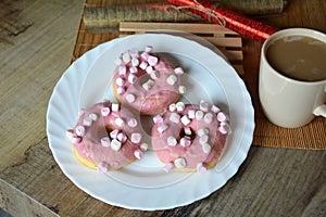 Cup of coffee with milk and three donuts with pink icing on a white plate.