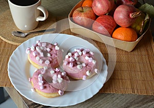 Cup of coffee with milk and three donuts with pink icing on a white plate.