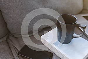 Cup of coffee with mobile phone on sofa in living room