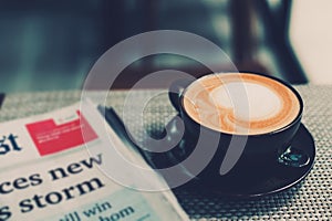 A cup of coffee and a newspaper of coffee on a wooden table