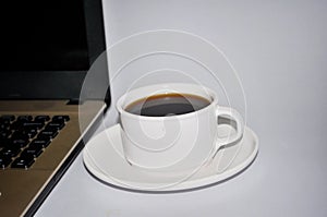 Cup of coffee next to computer note book on white background