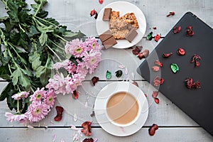 A Cup of coffee,note book , cracker, cookie, biscuit, lupins flowers on a wooden table.