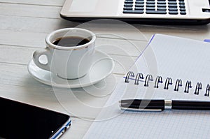 Cup of coffee, notebook with pen and laptop on white desktop