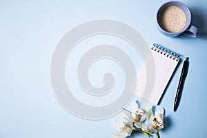 Cup of coffee and notebook with pen and orchid flower on a blue background, top view