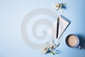 Cup of coffee and notebook with pen and orchid flower on a blue background, top view