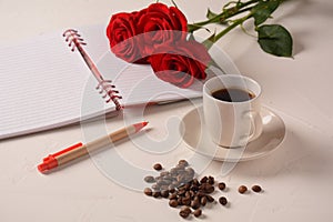 Cup of coffee, notebook, pen and rose flowers.