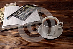 Cup of coffee and notepad with dollars, pencil and calculator on wooden desk. Financial concept