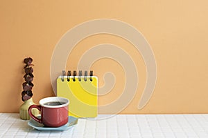 Cup of coffee and notepad, dry eucalyptus on white table. orange wall background. copy space