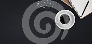 A cup of coffee, notepads, a calculator on a black background, top view.