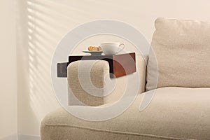 Cup of coffee and nut shaped cookies on sofa with wooden armrest table indoors. Interior element