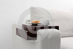 Cup of coffee and nut shaped cookies on sofa with wooden armrest table indoors. Interior element