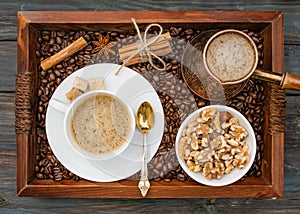 Cup of coffee, nuts in the bowl, coffeepot, cinnamon, anise, sugar, coffee beens on a wooden tray. Flat Lay with no people. View f