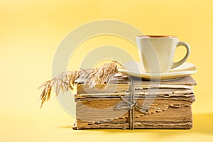 A cup of coffee on old books and dry ears of corn in yellow. Wellness, harmony, quiet reading. Copy space