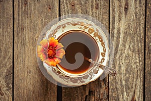 a cup of coffee with one red flower on handles on a wooden background, coffee