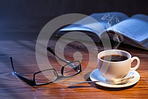 Cup of coffee, open book and glasses on a desk.