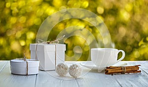 Cup of coffee outdoor with coconut candy balls sunshine on a white wooden board and boxes