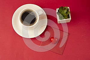 Cup of coffee over deep red background with red letter, decorative heart and plant. Top view. Valentine's Day concept